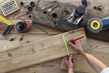 hands carpenter work the wood, measuring with tape meter and pencil old rustic wooden boards, top view with tools on background