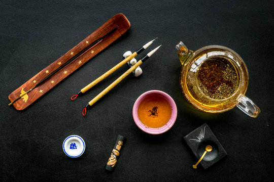 Chinese or japanese traditions. Calligraphy and tea ceremony concept. Special writting pen, ink near teapot and cup of tea, insense on black background top view