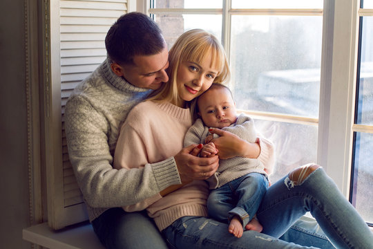 Family In Warm Sweaters With His Son Sitting On The Window In The Winter