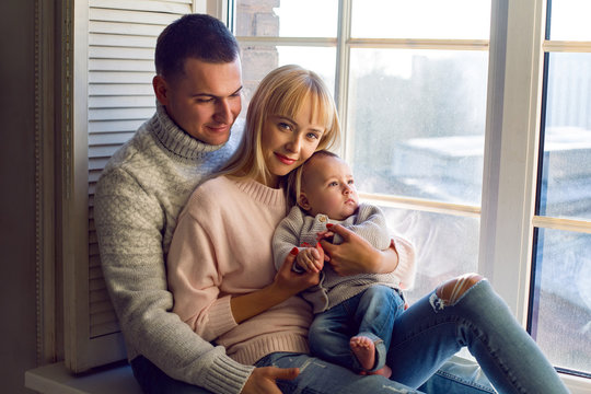 Family In Warm Sweaters With His Son Sitting On The Window In The Winter