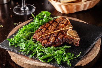 The concept of Italian cuisine. Juicy T-bone steak of beef aging stewed meat, with rucola salad and cherry tomatoes. A glass of red wine and bread basket on the table