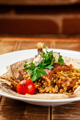 The concept of Eastern, Turkish, Uzbek cuisine. Pilaf with pieces of meat is served in pita bread, in a white plate on a wooden table. parsley and vegetables on the table.