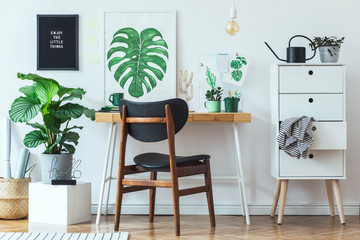 Stylish scandinavian open space with  office desk with mock up poster frames, a lot of plants and office accessories. Brown wooden parquet and white backgrounds wall. Floral concept of interior decor.