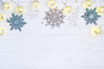 Christmas and New Year wooden background with light festive golden decoration garland with christmas balls and toys on white wooden background, top view