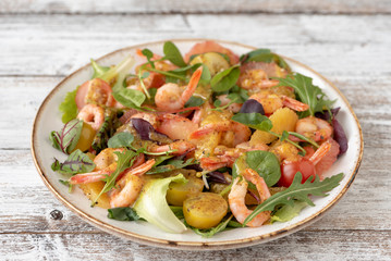 salad with shrimps and assorted salads (arugula, cherry tomatoes, chard, spinach) on white wooden background