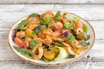 salad with shrimps and assorted salads (arugula, cherry tomatoes, chard, spinach) on white wooden background