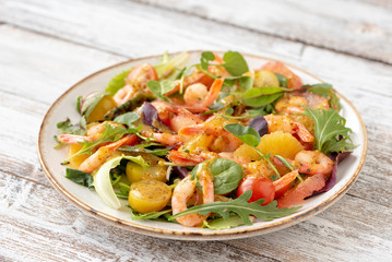 salad with shrimps and assorted salads (arugula, cherry tomatoes, chard, spinach) on white wooden background