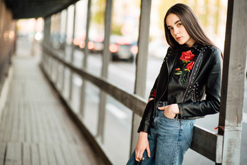 Obraz na płótnie Canvas Portrait young punk rock fashion girl in a black leather jacket with stilettos in an urban environment of a street warehouse, woman in jeans walking