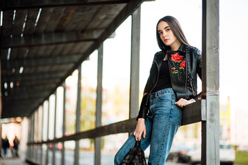 Portrait young punk rock fashion girl in a black leather jacket with stilettos in an urban...