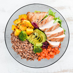 Bowl Buddha. Buckwheat, pumpkin, chicken fillet, avocado, carrots. On a white wooden background. Top view. Free space for your text.