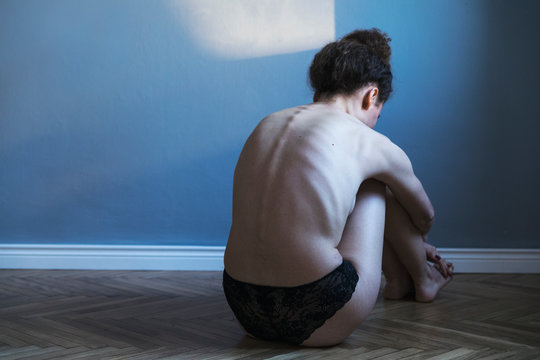 Young woman with anorexia and depression sitting alone on the flor in gray room. Sadness, nostlagic, depression. Mental problems of young people.
