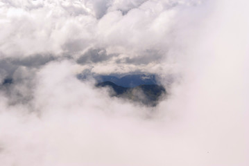 top view of white cumulus clouds; mountain peaks are visible in a small gap in the clouds