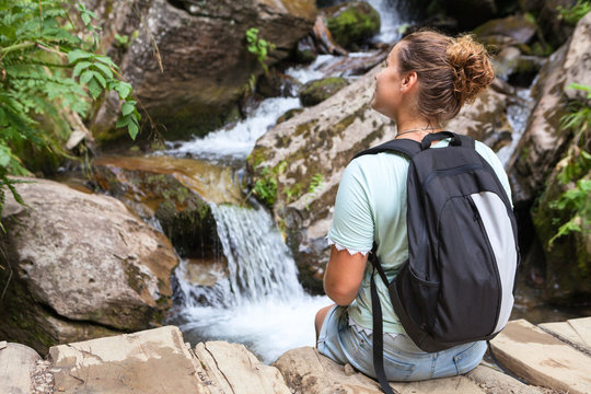 Woman sits on rock and admires the beautiful views of mountain waterfall, copyspace