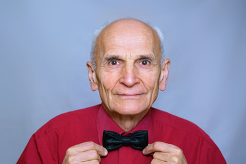 portrait of a senior old man holding a black bow-tie on a red shirt