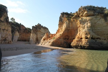 Fototapeta na wymiar Beautiful view of a sunny beach with crystal clear blue water and fine white sand next to a steep rocky cliff in Lagos, Algarve, Portugal