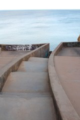 Sun setting over the deep blue ocean, seen from a concrete construction with steps leading down to the beach