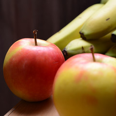 Apfel rot und gelb vor Staude Bananen und dunklem Hintergrund
