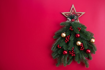Christmas background concept. Top view of Christmas tree with spruce branches, pine cones, red berries and golden star on red background.
