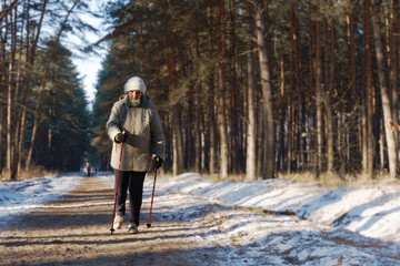 Active senior lady engaged in Nordic walking with sticks in the winter forest