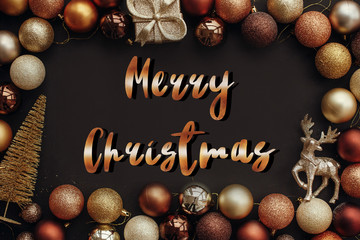 Merry Christmas text, handwritten golden sign at christmas gold frame of gift box, tree, reindeer and glitter baubles on stylish black background. Seasons greetings card