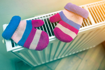 Children's warm hand knitted striped woolen gloves drying on heating radiator after winter day...