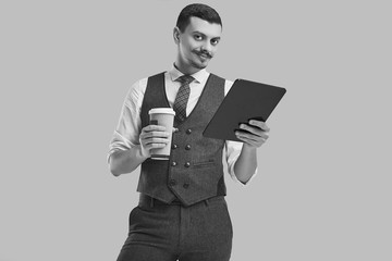 Handsome young arabic businessman in brown suit holds tablet and coffee