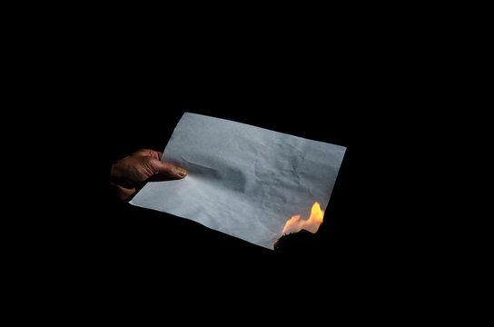 Burning sheet of paper in the male hand.