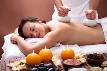 Fototapeta na wymiar Therapist Giving Massage With Herbal Compress Balls To Woman