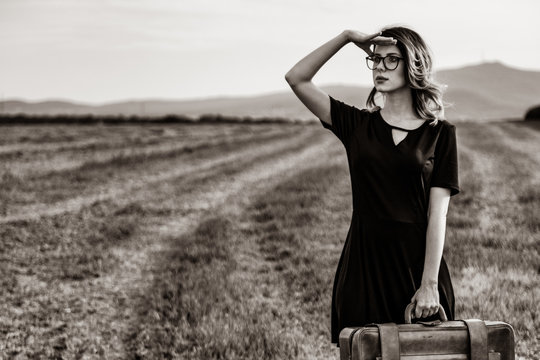 Portrait of young woman in black dress at autumn countryside with suitcase. . Image in black and white color style