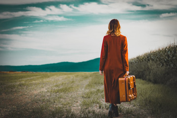 Portrait of young woman in red coar at autumn countryside with suitcase.