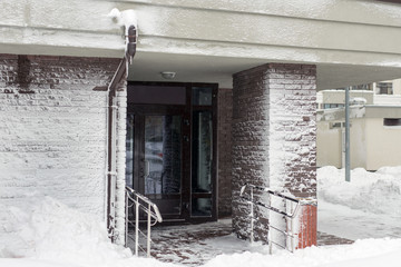Entrance of modern high-rise apartment building covered with snow and frost after heavy windy snowstorm Snowfall and blizzard aftermath in winter. Cold snowy weather forecast