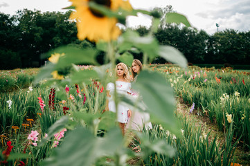 Fototapeta na wymiar Two pretty young female friends in ethnic dresses relaxing in flower garden in summer. Couple of cute barefoot women in country embroidery holding hands and hugging outdoor. Stylish fashionable girl