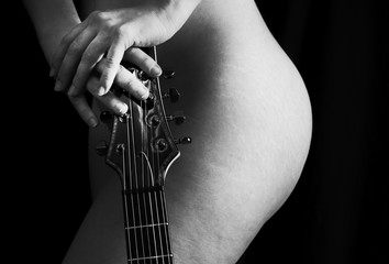 attraktiver sexy nackter Körper einer jungen wunderschönen Frau, Hüfte und Hände, welche den Gitarrenhals halten, schwarzweiß Bild - obrazy, fototapety, plakaty