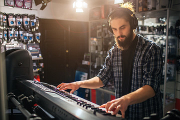 Serious and concentrated young man playing on keyboard. He listen to music through headphones. It is sunny inside.