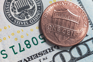 Macro photo of one cent and 100 US dollars on the background. Reverse american coin 2016 face value 1 cent photographed very close.