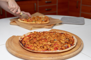 Baking a delicious pizza in a home kitchen. Slicing and stacking the baked pizza on the kitchen table.