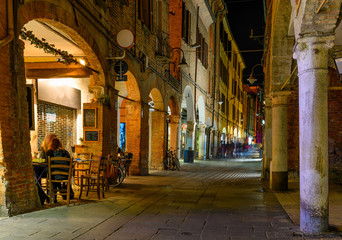 Fototapeta na wymiar Cozy narrow street at night in Ferrara, Emilia-Romagna, Italy. Ferrara is capital of the Province of Ferrara