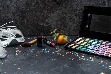 Image of christmas decoration, mandarin, brushes, lipstick, palette with shadows on black table