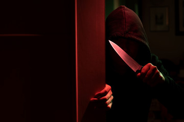 Image of killer with knife and in hood in dark apartment with red light