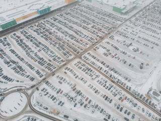 Aerial view of large automobile parking lot with many cars near mall or shopping center in winter with snow, drone photo