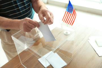 Elderly man putting ballot paper into box at polling station, closeup