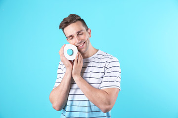 Young man holding toilet paper roll on color background