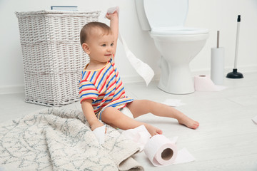 Cute toddler playing with toilet paper in bathroom