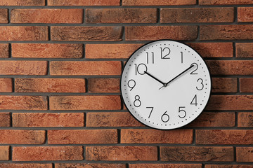 Stylish analog clock hanging on brick wall. Space for text