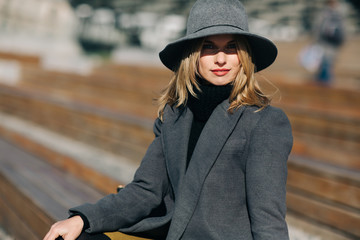Photo of young blonde in gray coat sitting on wooden bench