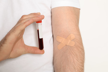 Man holding test tube near hand with adhesive plasters against white background, closeup. Blood donation concept