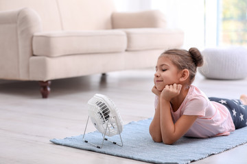 Little girl relaxing in front of fan at home. Summer heat
