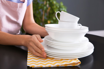 Woman with clean dishes on table in kitchen, closeup