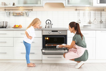 Young woman and her daughter baking cookies in oven at home