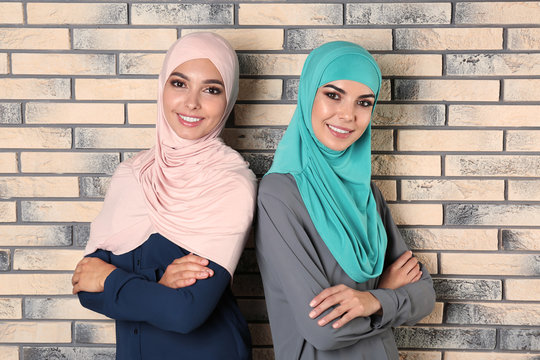 Portrait of young Muslim women in hijabs against brick wall